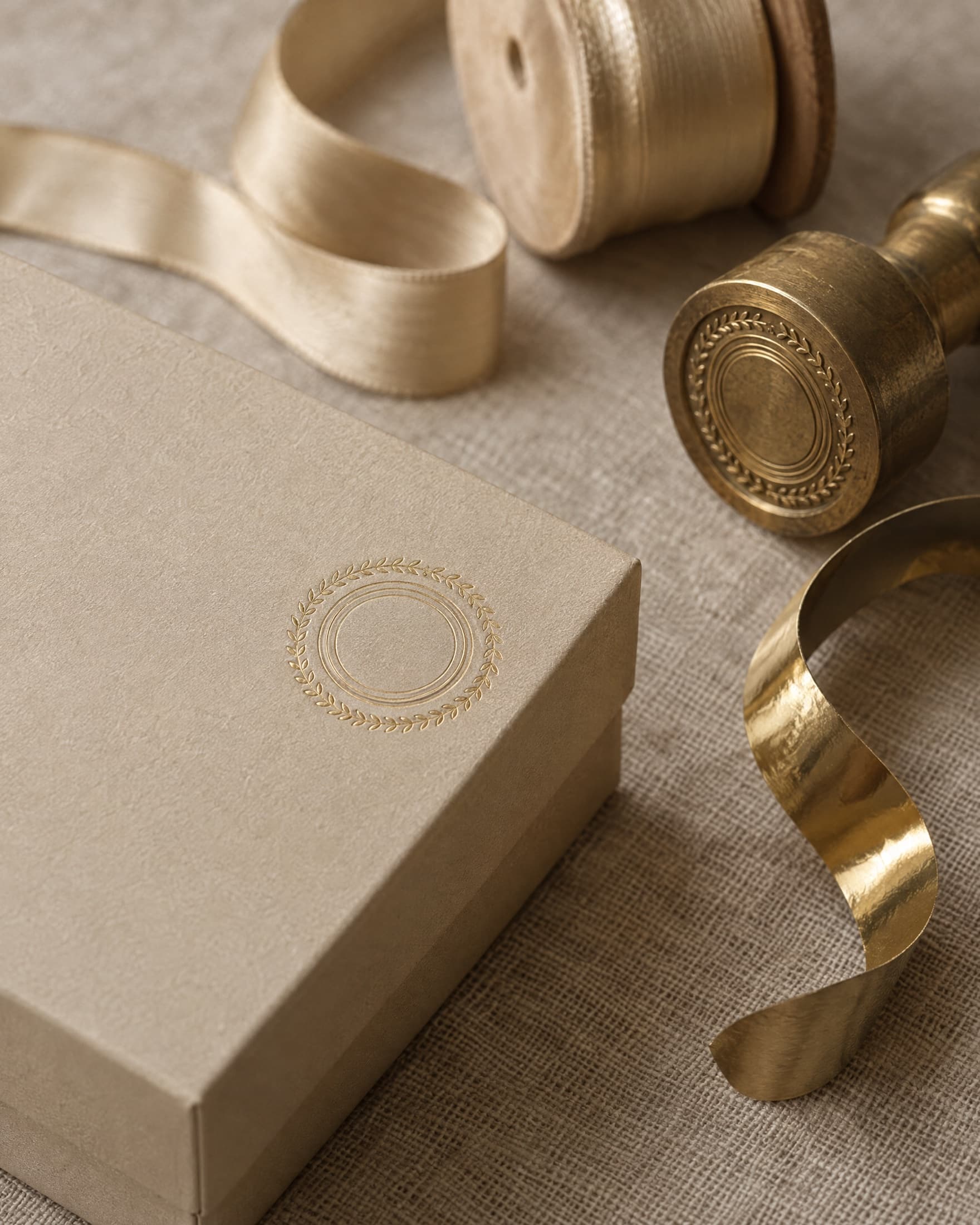 A gold-foil crest stamped on a champagne box lid, beside a brass stamping die and gold ribbon